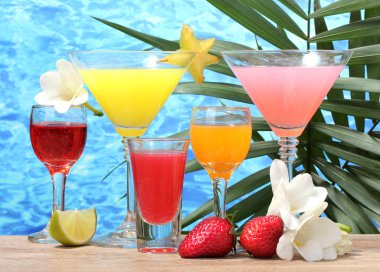 Exotic cocktails and flowers on table on blue sea background clipart