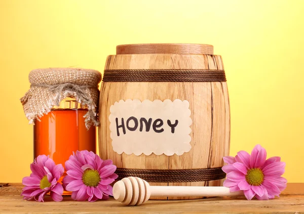Süßer Honig im Fass und Glas mit Nieselregen auf Holztisch auf gelbem Hintergrund — Stockfoto