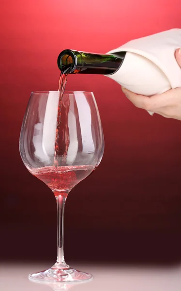 Pouring wine into wineglass on red background — Stock Photo, Image