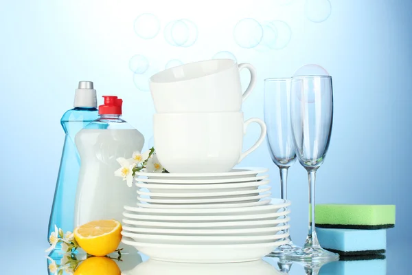 Üres tiszta tányérok, poharak és csészék és folyékony mosogatószer, szivacsok és a citrom, a kék háttér — Stock Fotó