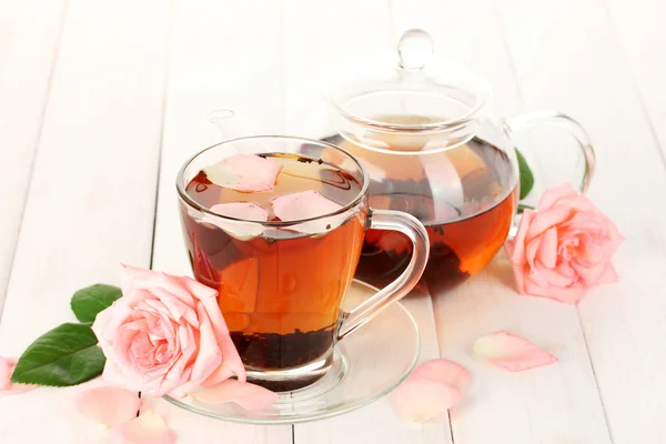 Tetera y taza de té con rosas sobre mesa de madera blanca —  Fotos de Stock