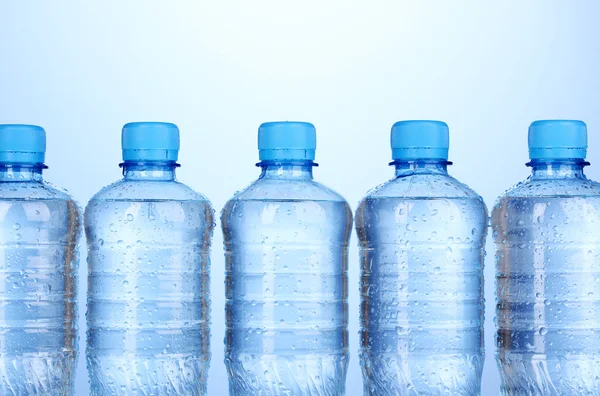 Plastikflaschen mit Wasser auf blauem Hintergrund — Stockfoto