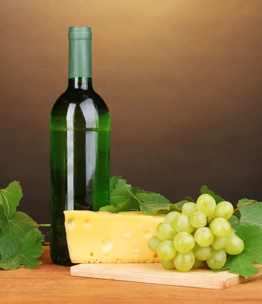 Flasche großer Wein mit Glas und Käse auf Holztisch auf braunem Hintergrund — Stockfoto