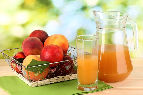 Ripe peaches and juice on wooden table on natural background — Stock Photo, Image