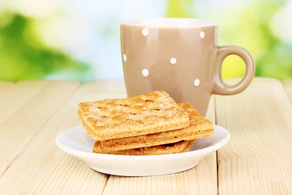 Xícara de chá e biscoitos na mesa de madeira no fundo brilhante — Fotografia de Stock