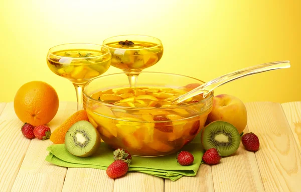Soco em tigela e copos com frutas, na mesa de madeira, no fundo amarelo — Fotografia de Stock