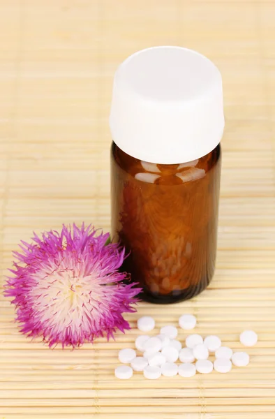 Medicine bottle with tablets and flower on bamboo mat — Stock Photo, Image