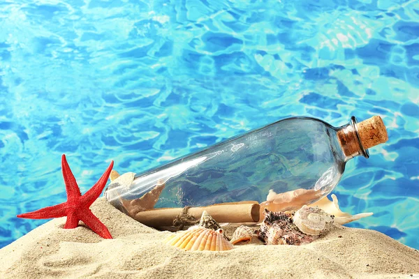Glasflaska med en märka insida på sand, på blå havet bakgrund — Stockfoto