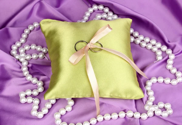 Anelli nuziali su cuscino di raso su sfondo di stoffa viola — Foto Stock