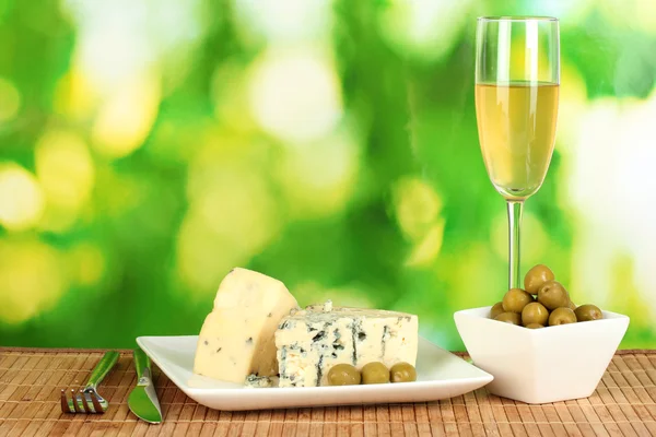 Samenstelling van blauwe kaas, glas wijn en olijven op helder groene achtergrond close-up — Stockfoto