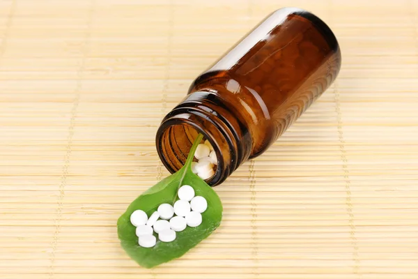 Пузырек с таблетками на зеленом листе на бамбуковом коврике — стоковое фото