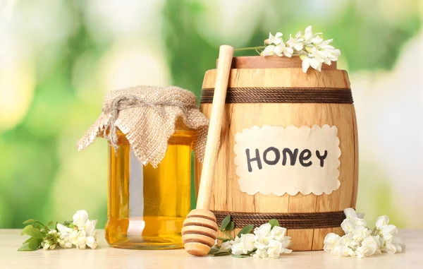 Miel dulce en barril y tarro con flores de acacia sobre mesa de madera sobre fondo verde —  Fotos de Stock