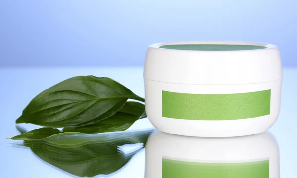 Vaso di crema con foglie verdi su sfondo blu — Foto Stock