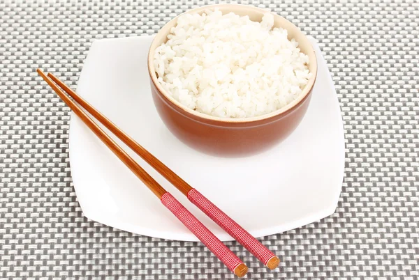 Ciotola di riso e bacchette su piatto su tappetino grigio — Foto Stock