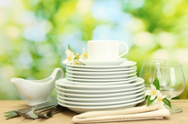 Empty clean plates, glasses and cup on wooden table on green background clipart