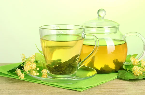 Tetera y taza con té de tilo y flores sobre mesa de madera sobre fondo verde — Foto de Stock