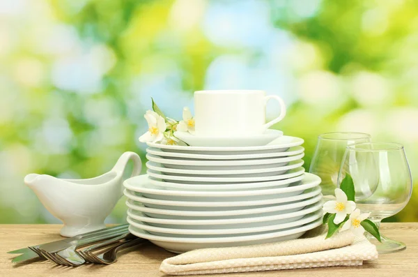 Leere saubere Teller, Gläser und Tassen auf Holztisch auf grünem Hintergrund — Stockfoto