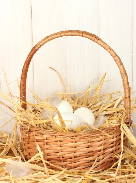 White eggs in a wicker bascet on straw on white wooden background — Stock Photo, Image