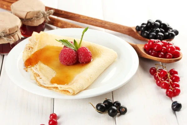 Вкусный блин с ягодами и медом на тарелке на деревянном столе — стоковое фото