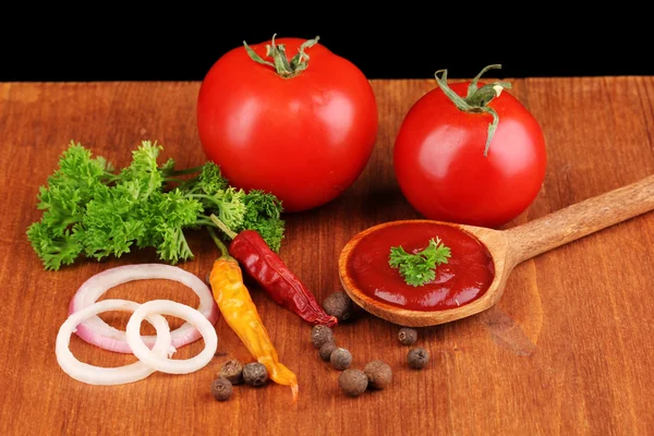 Ketchup and ripe tomatoes on wooden table on black background — Stock Photo, Image