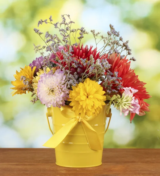 Bright yellow bucket with flowers on green background — Stock Photo, Image