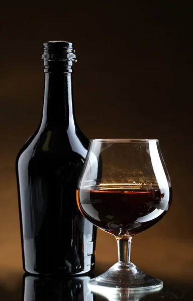Стакан бренди и бутылка на коричневом фоне — стоковое фото