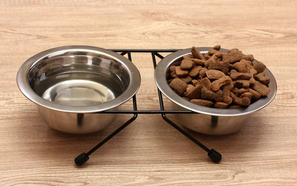 Hond droog voedsel en water in metalen kommen op houten achtergrond — Stockfoto