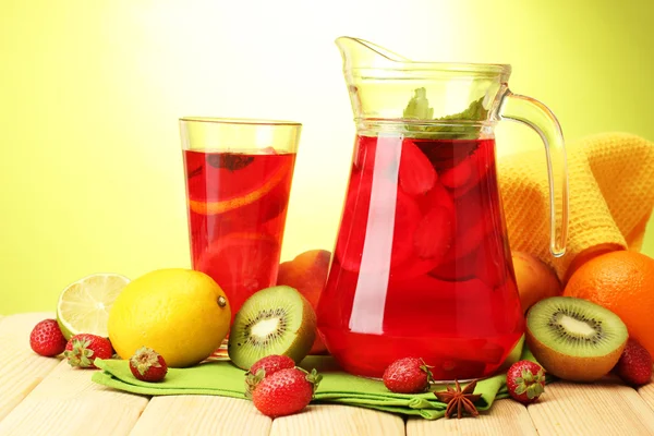 Sangria sklenice a sklo s ovocem, na dřevěný stůl, na zeleném pozadí — Stock fotografie