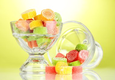 Colorful jelly candies in in glass bowls on green background clipart