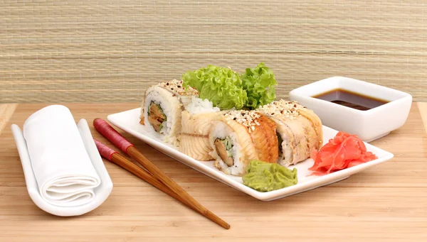 Deliciosos rollos servidos en plato blanco con palillos sobre mesa de madera sobre fondo claro — Foto de Stock