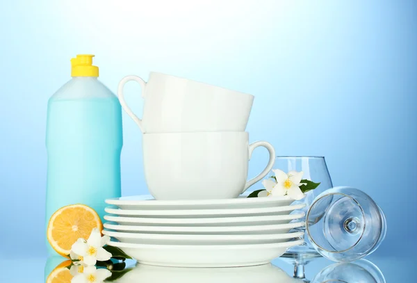 Порожні чисті тарілки, окуляри та чашки з посудомийною рідиною та лимоном на синьому фоні — стокове фото