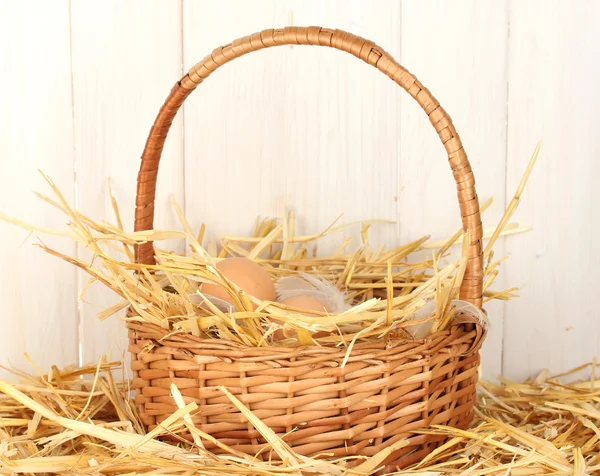 Braune Eier in einem Weidenkorb auf Stroh auf weißem Holzhintergrund — Stockfoto