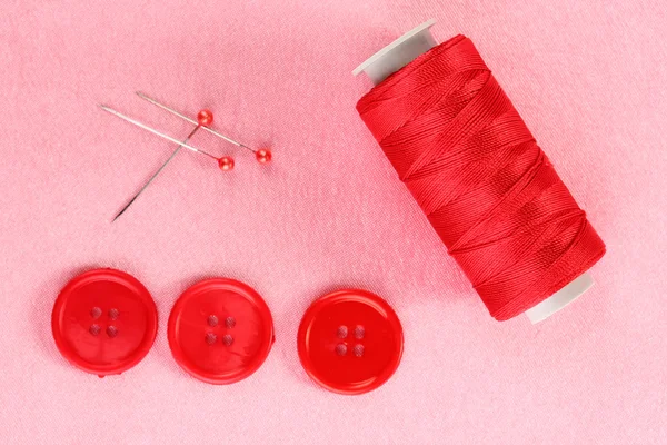 Цветные швейные пуговицы с ниткой на розовой ткани — стоковое фото