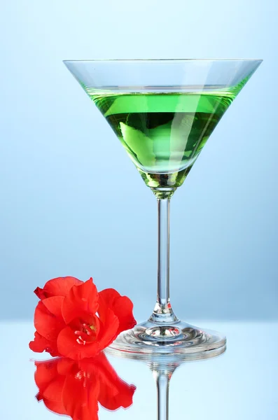 Glass with cocktail and gladiolus bud on blue background close-up — Stock Photo, Image