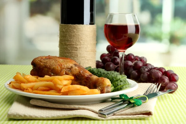 Жареная курица с картошкой фри и огурцами, бокал вина на зеленой скатерти в интерьере кафе — стоковое фото
