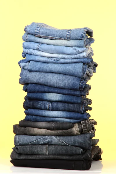 Molti jeans impilati in una pila su sfondo giallo — Foto Stock