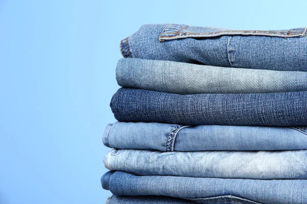 Многие джинсы сложены в кучу на синем фоне — стоковое фото