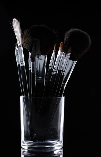Пензлі для макіяжу в скляній чашці на сірому фоні — стокове фото