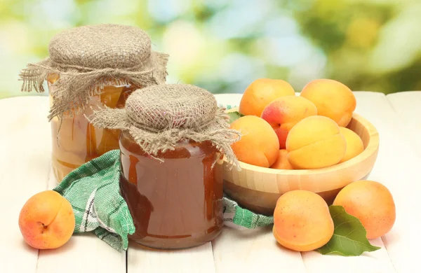 Konserverade aprikoser och sylt i en burkar och mogna aprikoser i skål på träbord på grön bakgrund — Stockfoto
