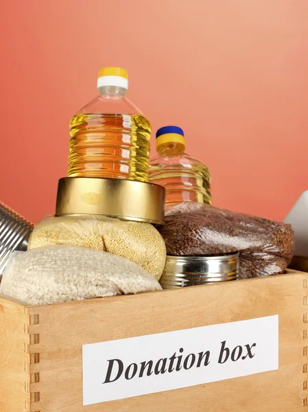 Spendenbox mit Lebensmitteln auf rotem Hintergrund in Großaufnahme — Stockfoto