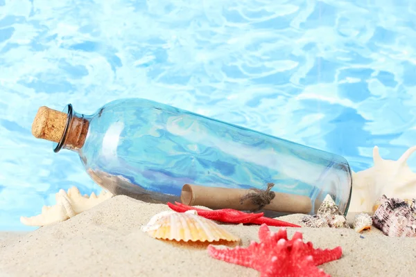 玻璃奶瓶与内部在沙子上，蓝色的大海背景上的笔记 — 图库照片