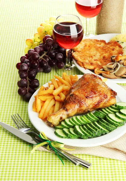 Roast chicken with french fries and cucumbers, glasses of wine on green table cloth — Stock Fotó