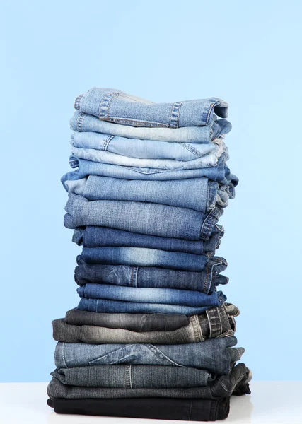 Muitas calças de ganga empilhadas em uma pilha no fundo azul — Fotografia de Stock