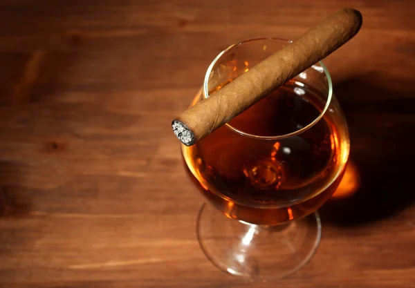 Vaso de brandy y cigarro sobre mesa de madera —  Fotos de Stock