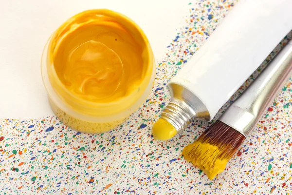 Pincéis com tinta colorida, tubo com aquarela e frasco com guache em salpicos coloridos fundo close-up — Fotografia de Stock