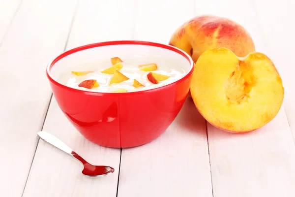 Yogurt dengan buah persik di mangkuk dengan latar belakang kayu — Stok Foto