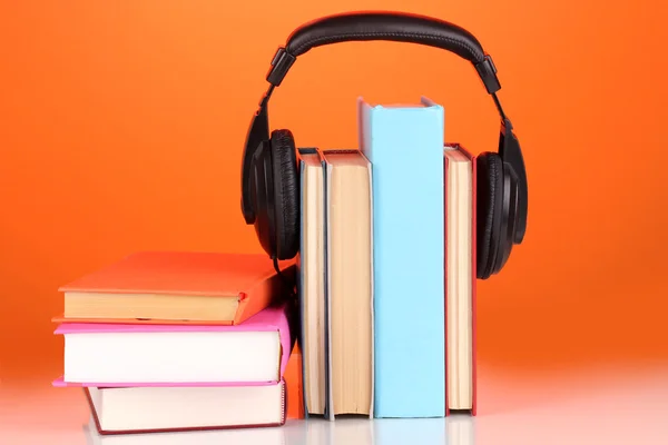Hörlurar på böcker om orange bakgrund — Stockfoto