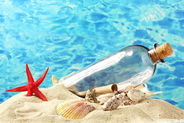 Butelki z Uwaga wewnątrz na piasku, na tle błękitnego morza — Zdjęcie stockowe