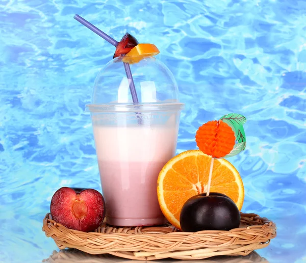 Вкусный молочный коктейль с фруктами на плетеной колыбели на синем фоне моря — стоковое фото