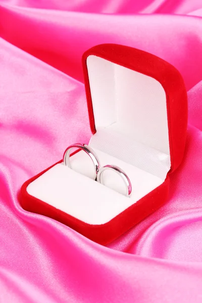 Anéis de casamento em caixa vermelha no fundo pano rosa — Fotografia de Stock